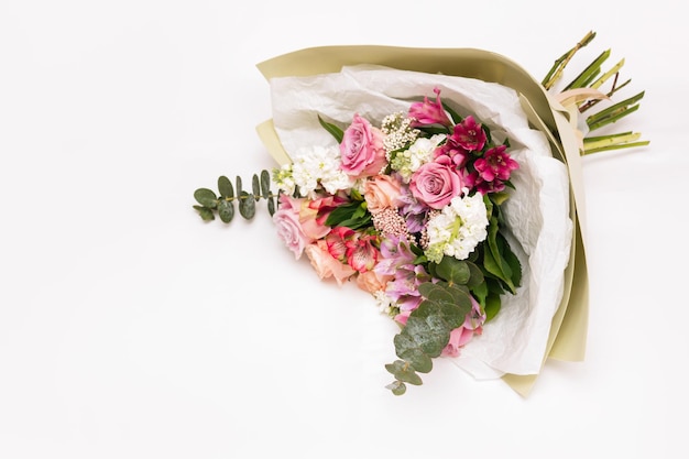 Blumenstrauß aus rosa und orangefarbenen Rosen in einem stilvollen festlichen Paket auf weißem Hintergrund Draufsicht