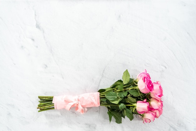 Blumenstrauß aus rosafarbenen Rosen, eingewickelt in rosa Geschenkpapier mit einem rosa Band auf Betongrund