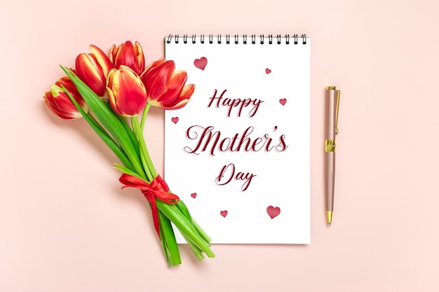 Blumenstrauß aus roten Tulpen text Happy Mother's Day auf offenem weißen Notizblock auf rosa Hintergrund