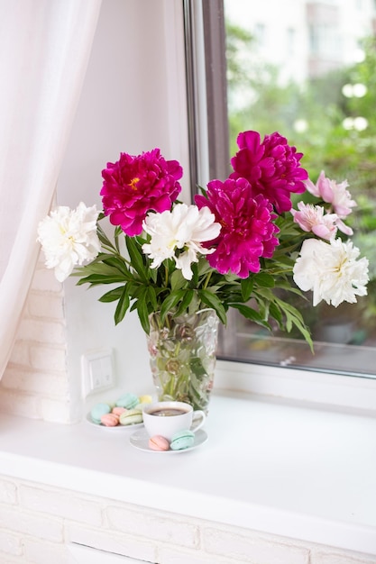 Blumenstrauß aus schönen rosa Pfingstrosen in einer Vase auf dem Tisch in der Nähe des Fensters