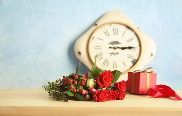 Blumenstrauß aus schönen Rosen und Uhr auf Holztisch