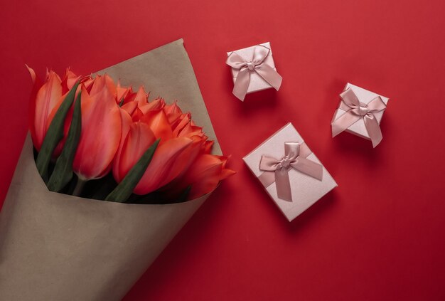 Blumenstrauß aus Tulpen und Geschenkboxen auf rotem Grund. Feiertag Muttertag oder 8. März, Geburtstag. Ansicht von oben