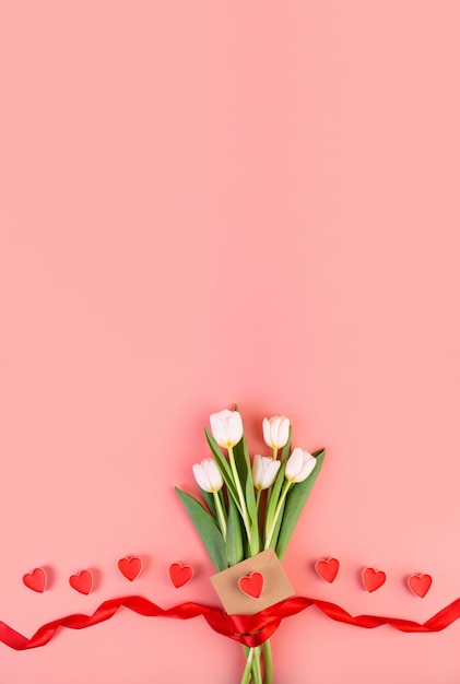 Blumenstrauß aus weißen Tulpen Herzen Umschlag Liebesbrief auf einem isolierten pastellrosa Hintergrund