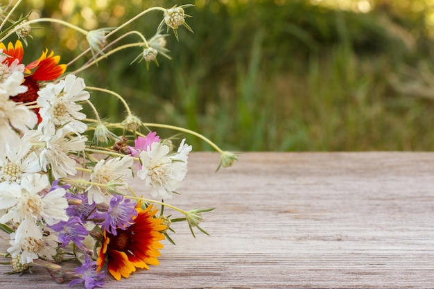 Blumenstrauß aus wildblumen auf altem holzbrett mit unscharfem natürlichen hintergrund.