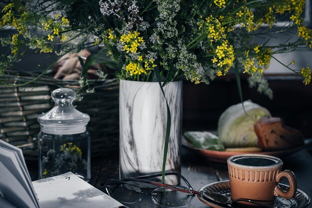 Blumenstrauß aus wilden Blumen, eine Tasse mit kaltem Tee, Brille und Notizbuch auf einem Holztisch in der Nacht