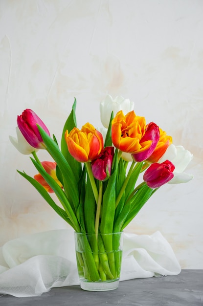 Blumenstrauß der bunten natürlichen Tulpen in einer Glasvase mit Wasser auf einem konkreten Hintergrund.