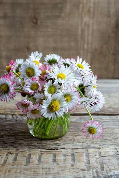 Blumenstrauß der gemeinsamen Gänseblümchen im Glas auf einem Holztisch