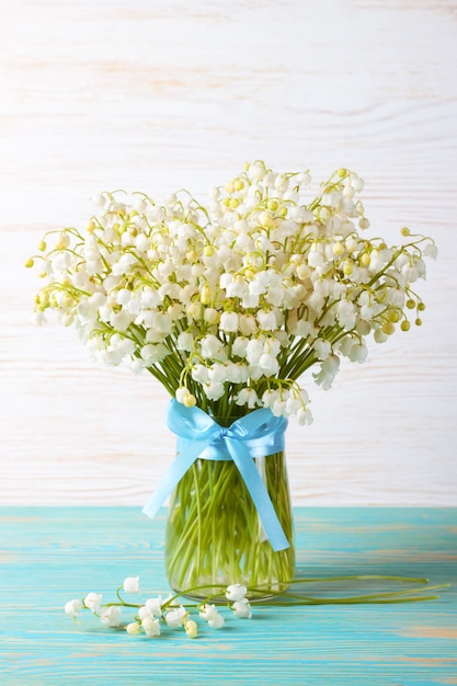 Blumenstrauß der Maiglöckchen in einer Vase mit blauem Band auf einem blauen und weißen hölzernen Hintergrund