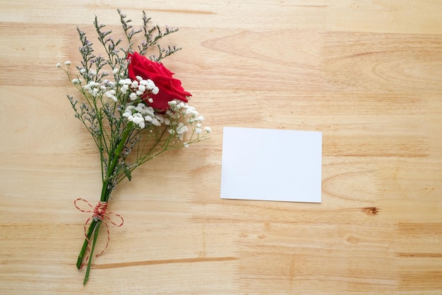 Blumenstrauß der roten Rosen und leeres weißes Briefpapier auf hölzernem Hintergrund