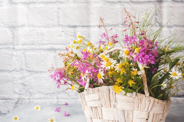 Blumenstrauß der schönen Wildblumen in einem Korb auf einem grauen Hintergrund mit Kopienraum.