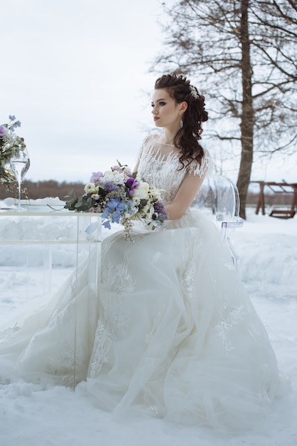 Blumenstrauß in den Händen der Braut, auf einem Stuhl sitzend. Winterhochzeitsfotografie