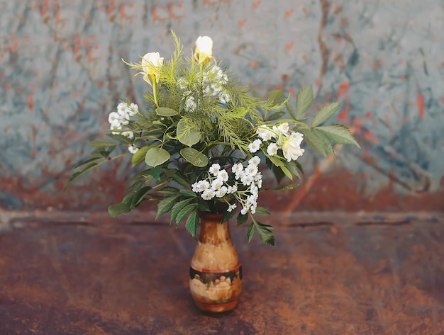 Blumenstrauß in der Holzvase mit grünen Blättern und weißen Rosen