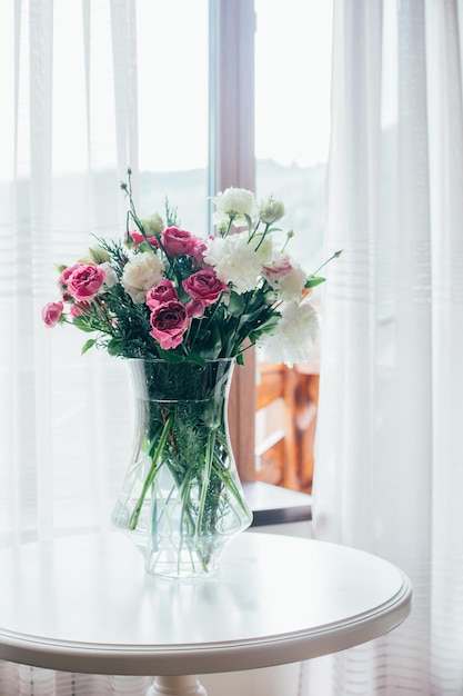 Blumenstrauß in einer transparenten Vase auf dem Tisch vor dem Hintergrund des Fensters