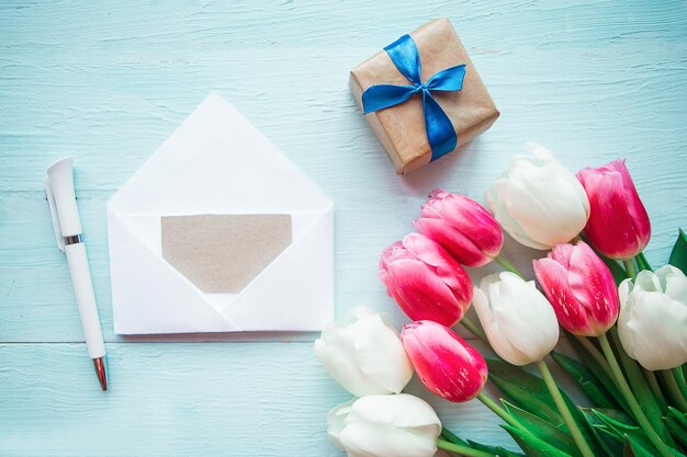 Blumenstrauß mit rosa und weißen Tulpen und Geschenkkiste auf Holzgrund Ostern- oder Muttertagsgrußkarte