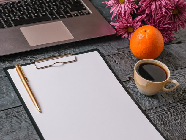 Blumenstrauß, Notizbuch, Tasse Kaffee, Orange und Stift auf dunklem rustikalem Tisch. Der Blick von oben.