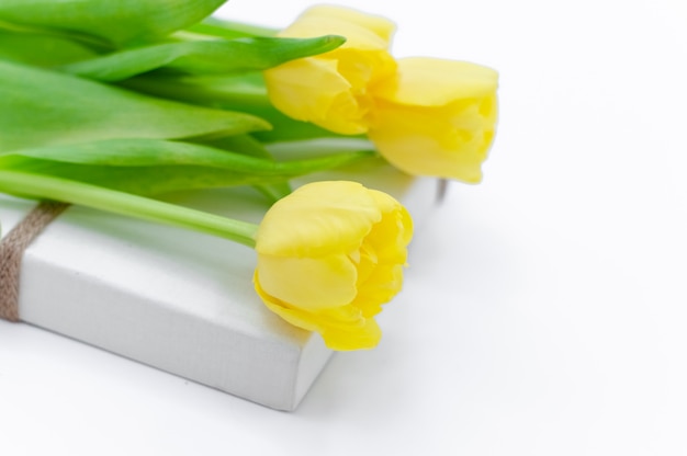 Blumenstrauß von den gelben frühlingstulpen, die auf der weißen geschenkbox lokalisiert auf weißem hintergrund liegen