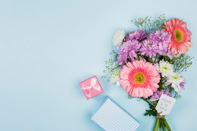 Blumenstrauß von frischen Blumen mit Titel auf Tag nahe Präsentkarton und Notizbuch