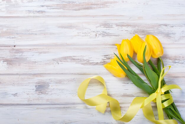 Blumenstrauß von gelben Tulpen und von Geschenk mit einem gelben Band auf einem hölzernen Hintergrund