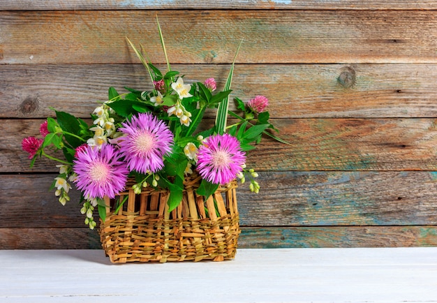 Blumenstrauß von Kleeblumen, von Kornblumen und von Jasmin im Weidenkorb auf weißem Holztisch