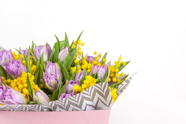 Blumenstrauß von lila Tulpen und gelben Mimosen in der rosa Box auf weißem Hintergrund, Kopienraum, Seitenansicht