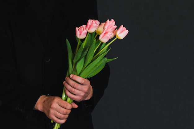 Blumenstrauß von rosa Tulpen in den Händen eines Mannes in einem schwarzen Mantel