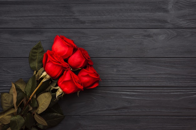 Blumenstrauß von roten Rosen auf einem dunklen hölzernen Hintergrund.