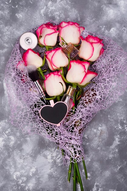 Blumenstrauß von schönen Rosen mit Kosmetik auf grauem Beton