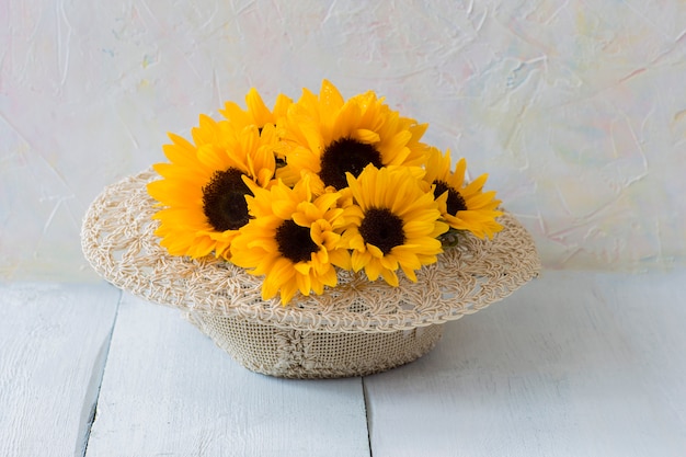 Blumenstrauß von Sonnenblumen in einem Strohhut auf einem weißen Holztisch