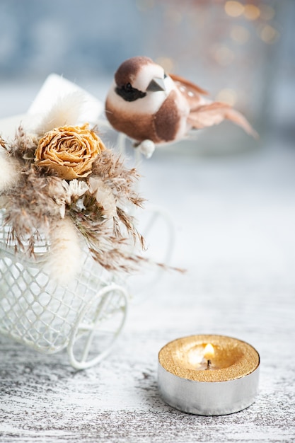 Blumenstrauß von trockenen Blumen auf dekorativem Fahrrad mit kleinem braunem Vogel und brennender Kerze auf dem Tisch. Grußkarte für Hochzeit oder Urlaub in natürlichen Tönen