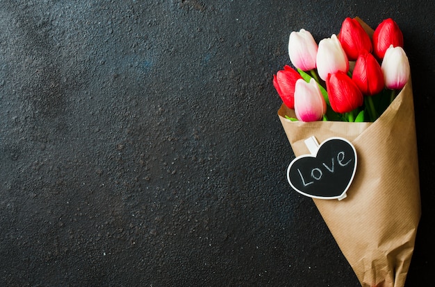 Blumenstrauß von Tulpen und von Geschenkbox auf dunklem Hintergrund.