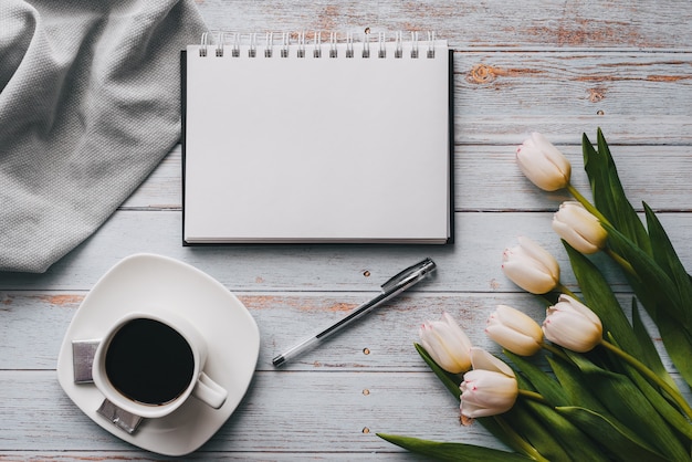 Blumenstrauß von weißen Tulpen mit einem leeren Notizbuch und einem Tasse Kaffee auf einem hölzernen Hintergrund