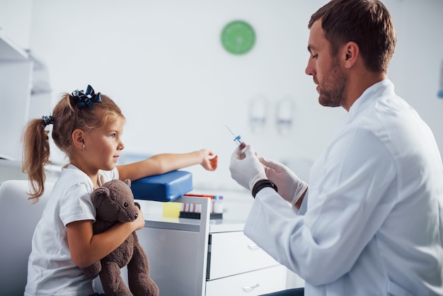 Blutprobe. Kleines Mädchen mit ihrem Teddybären ist mit Arzt in der Klinik.