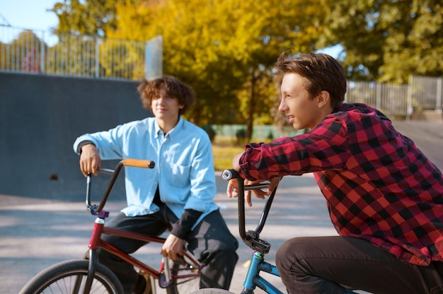 Bmx-fahrer auf fahrrädern, training auf der rampe im skatepark. extremer fahrradsport, gefährliche fahrradübungen, straßenreiten, teenager, die im sommerpark fahrrad fahren