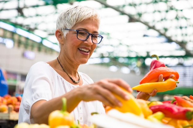 Boa aparência sênior mulher usando óculos compra pimenta no mercado