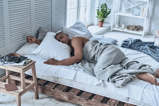 Boa soneca. Vista superior de um jovem africano dormindo deitado na cama em casa