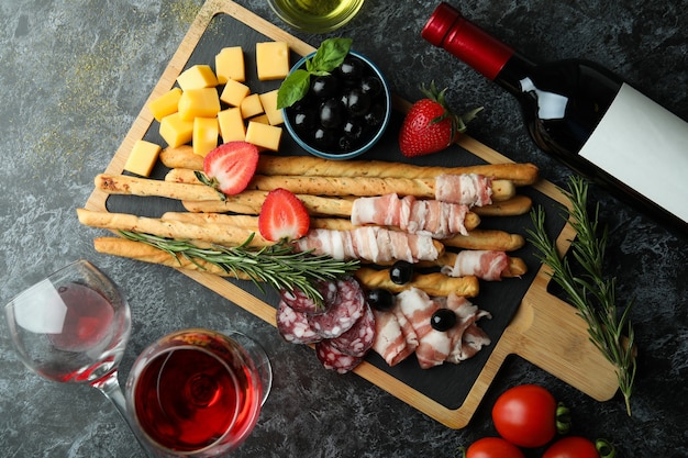 Board mit Grissini und Snacks und Wein auf schwarzer rauchiger Oberfläche