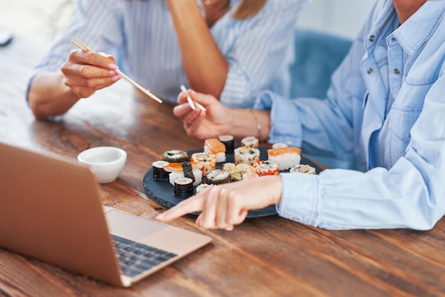 Boas duas garotas adultas em casa comendo sushi e trabalhando