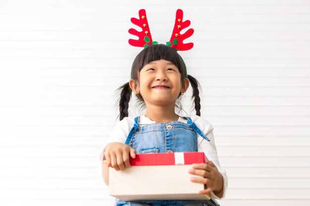 Boas festas e natal menina bonitinha alegre segurando a caixa de presente presente na sala de estar branca.