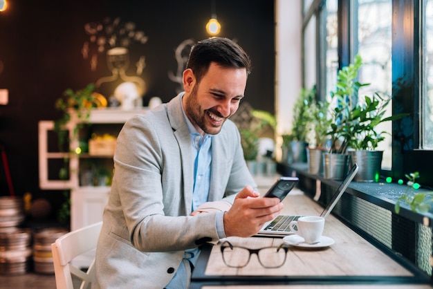 Boas notícias do colega. Homem de negócios novo que guarda o smartphone no café.