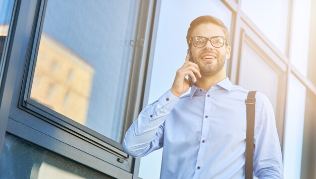 Boas notícias, jovem empresário caucasiano feliz de camisa azul, falando ao telefone e sorrindo enquanto