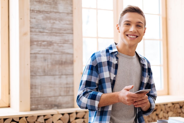 Foto boas notícias. menino bonito e exuberante de cabelos louros sorrindo, segurando o telefone e vestindo uma camisa xadrez