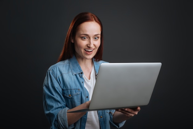 Boas notícias. Mulher otimista e idiota checando suas cartas e descobrindo novidades enquanto usa seu laptop