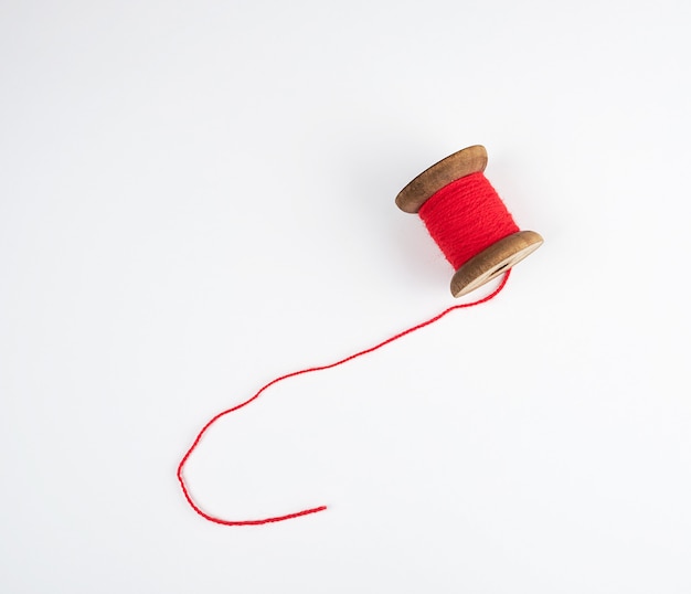 Foto bobina de madera con hilos de lana roja sobre blanco.