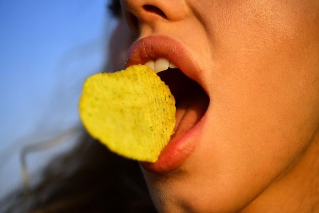 La boca femenina come papas fritas. Fichas con dientes, lengua y labios de cerca. Sabrosa comida rápida deliciosa. Comiendo patatas fritas. Comida rápida.