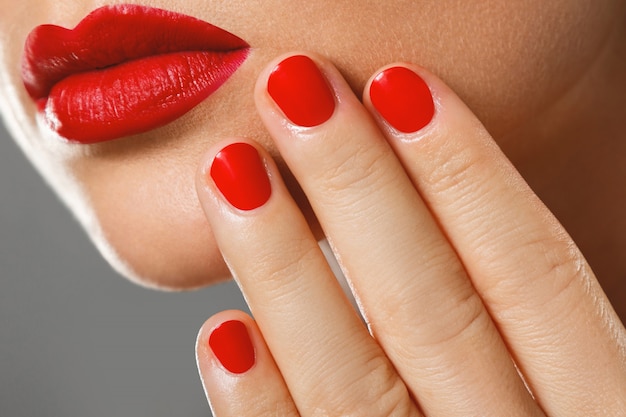 Boca femenina y uñas con manicura roja y lápiz labial.