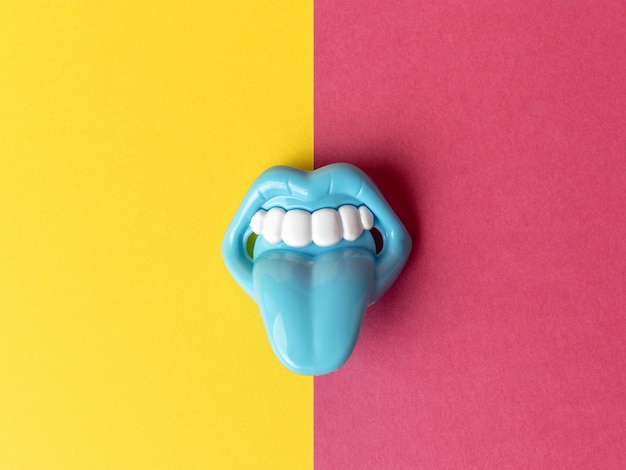 Boca de juguete azul con lengua sobresaliente en fondo dividido amarillo y rosa