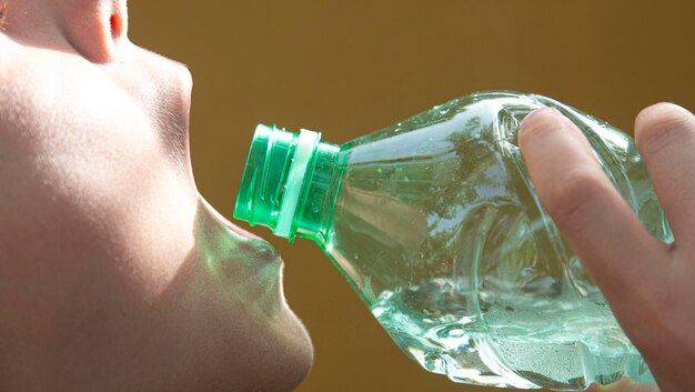 Boca de un niño de diez años bebiendo agua de una botella de plástico transparente