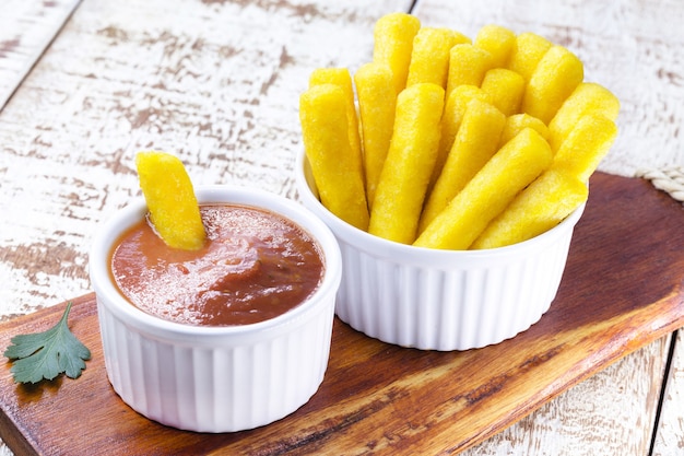 Bocadillo brasileño llamado polenta, servido con salsa y ketchup, superficie blanca aislada.