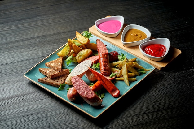 Bocadillo de cerveza clásico: salchichas de carne frita variadas, papas, pepinos encurtidos en un plato con salsas. Pub de comida