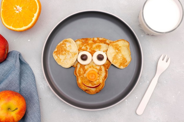 Bocadillo divertido con forma de cara de mono de panqueque en un plato Dulce postre saludable para niños lindos para niños Arte de comida para el almuerzo con leche Manzana Naranja sobre fondo de hormigón gris Vista superior